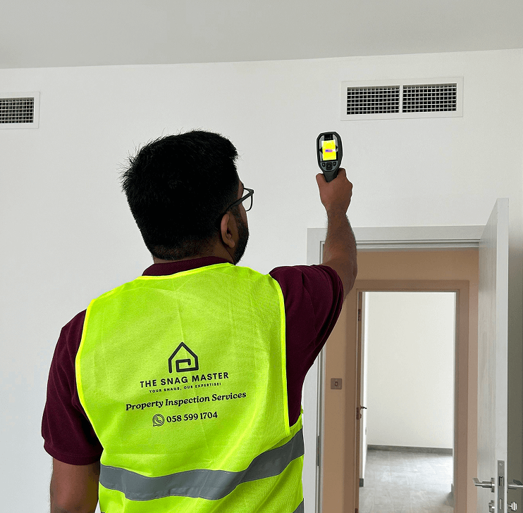 Property inspector using a handheld thermal scanner to check a ceiling inside a residential unit.